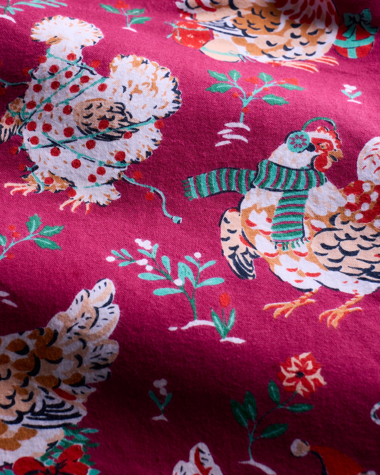 Close-up of the burgundy Holiday Hens print with chickens in winter accessories among flowers and greenery