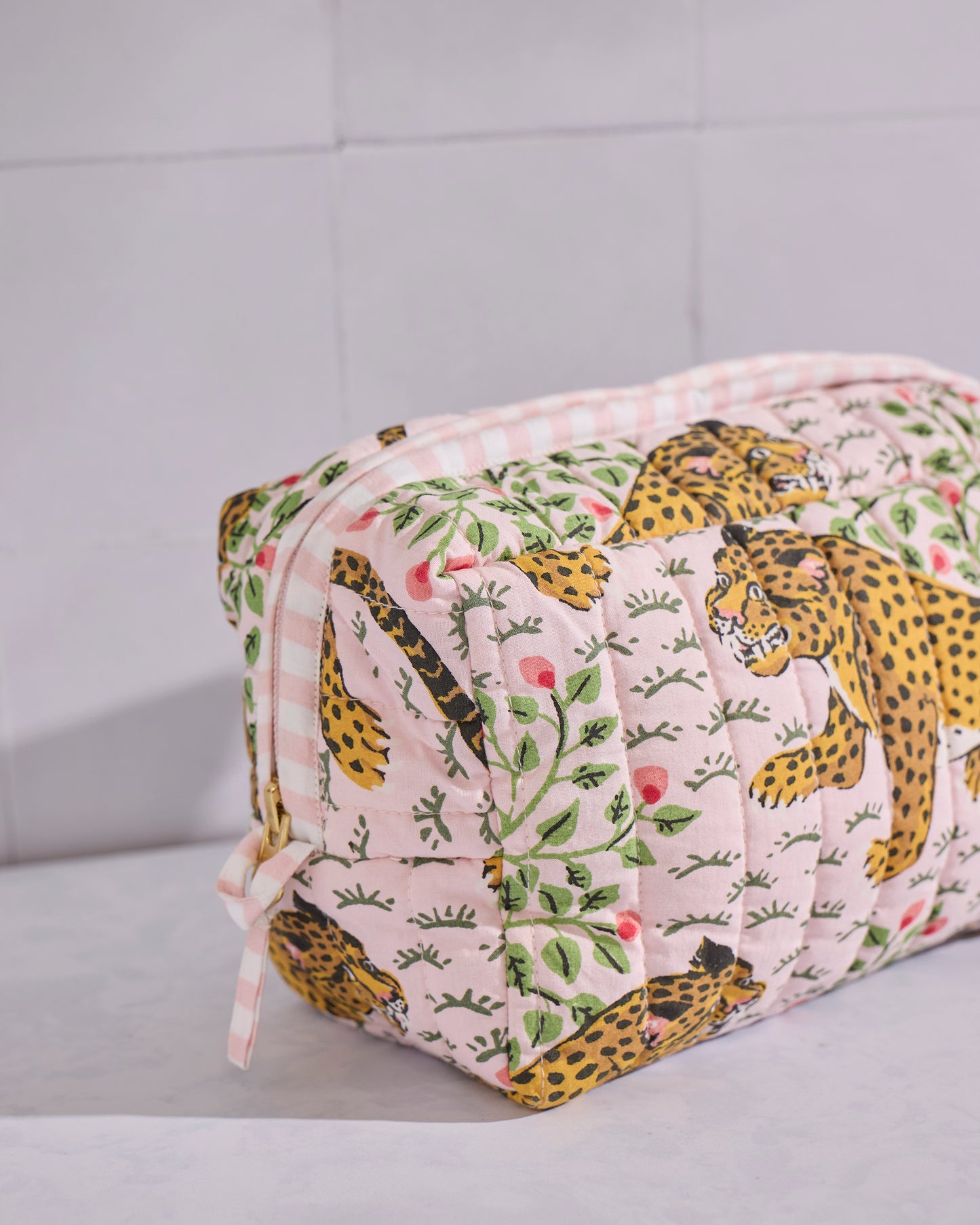 Angled close view of the pale pink quilted Bagheera pouch showing its zipper, side loop, and leopard-and-leaf print.