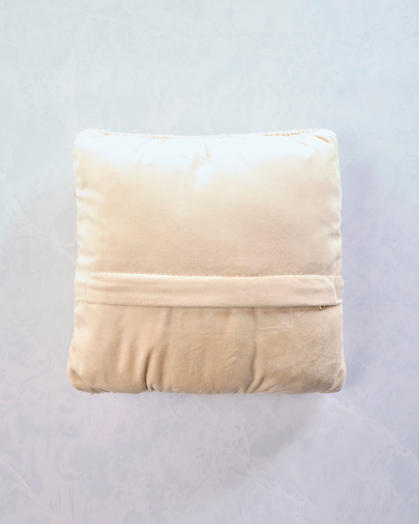 Back of the square red-and-cream striped pillow with a cream-colored backing and horizontal seam.