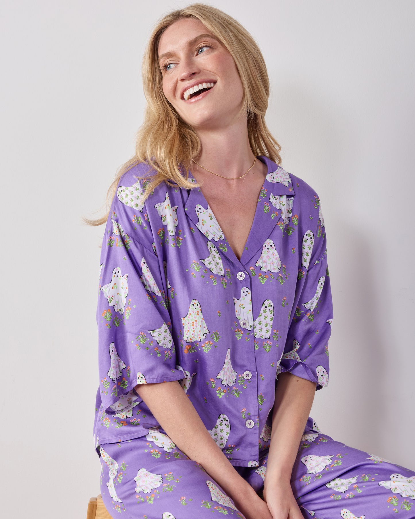 Seated close-up of the purple Gardening Ghosts pajama set showing the collared button-front top and matching printed pants.