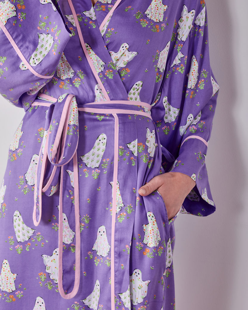 Close view of the purple ghost-and-floral print robe showing its pink-trimmed front, matching belt, and hand in a pocket.