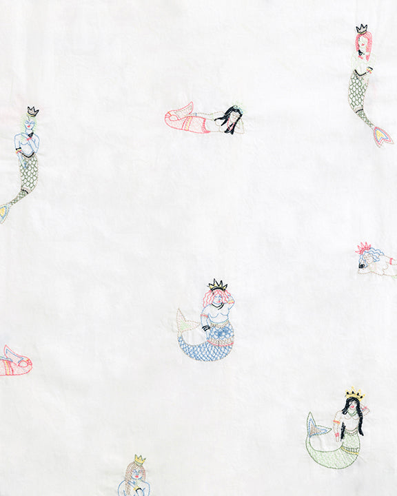 Close-up of the white pajama fabric with scattered embroidered mermaids in varied poses