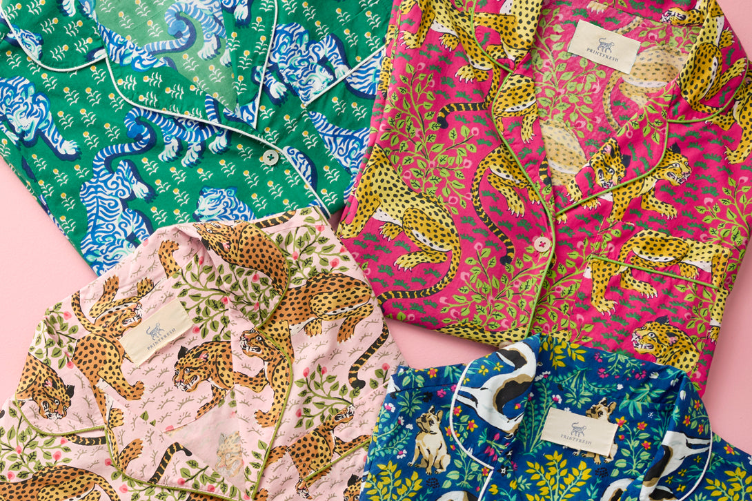 Four colorful patterned pajama tops arranged on a pink background.
