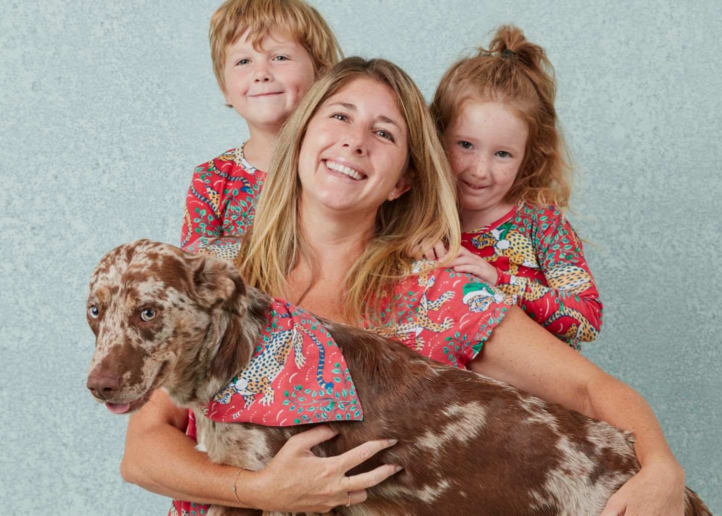 Adult and two children pose with a large dog against a textured blue-gray backdrop.
