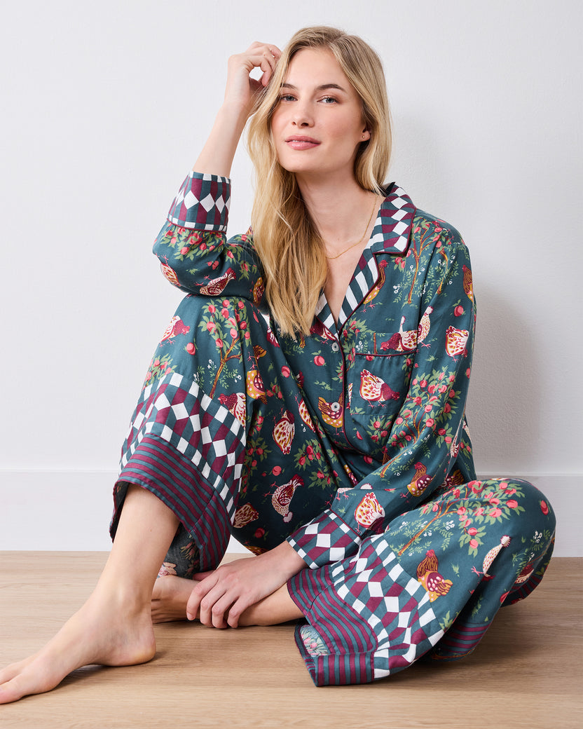 Seated front view of navy long-sleeve pajama set with chickens, fruit, flowers, and patterned trim