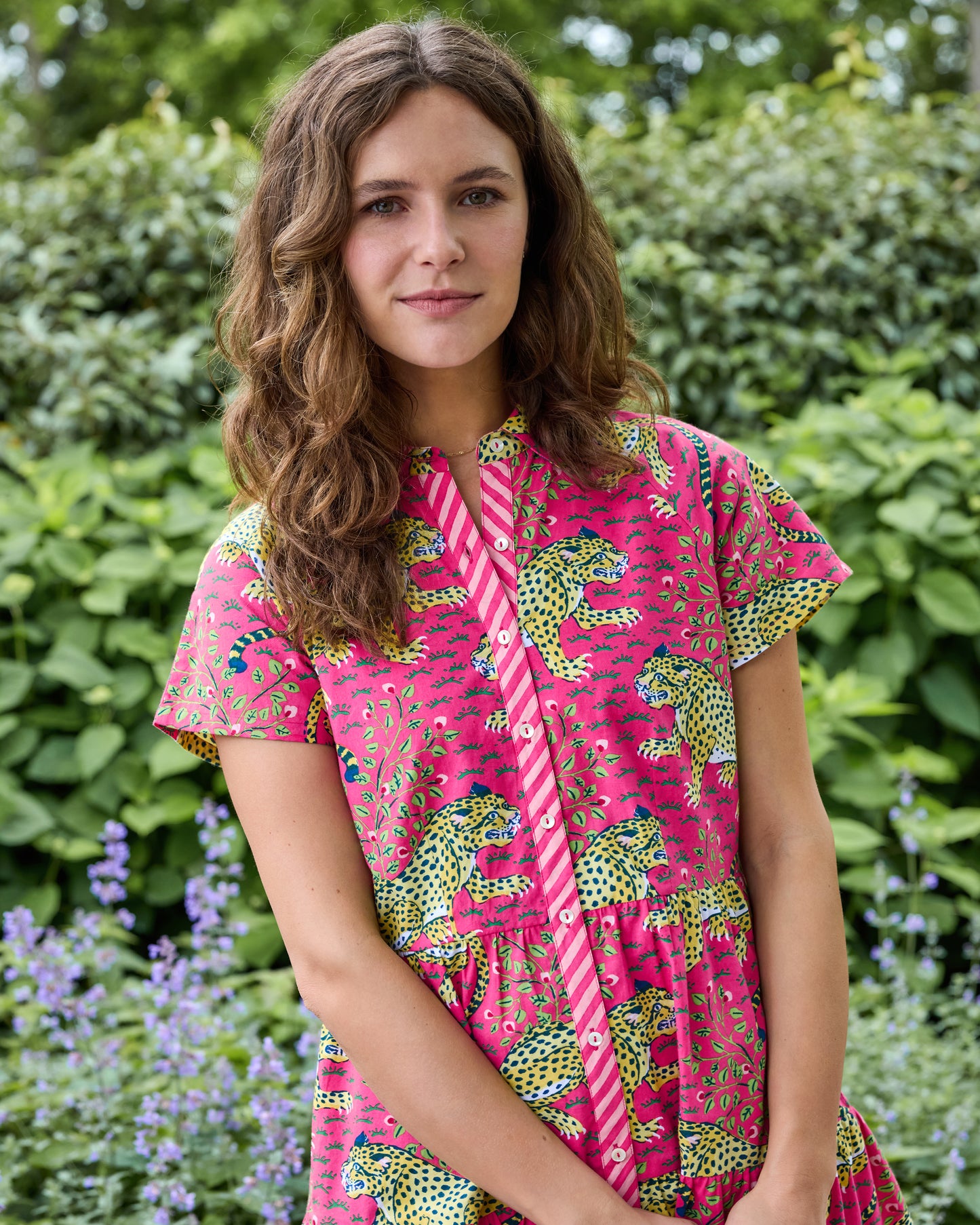 Model wearing a hot pink short-sleeved dress with a leopard and botanical print, shown from the waist up in a garden.