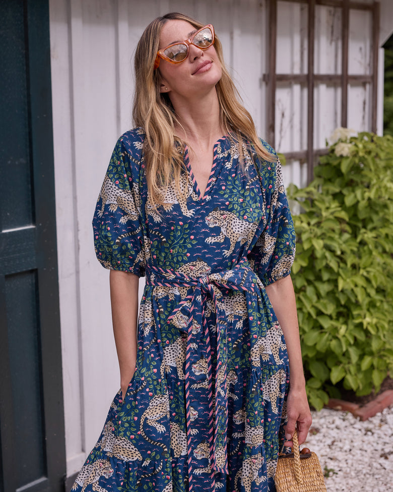 Front view of the navy Bagheera dress with leopard-and-floral print, tied belt, puff sleeves, and a woven handbag.