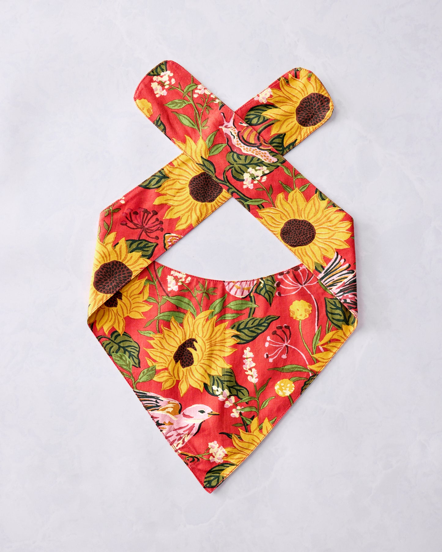 Orange pet bandana with a sunflower, bird, leafy floral, and butterfly print, laid flat with crossed neck straps.