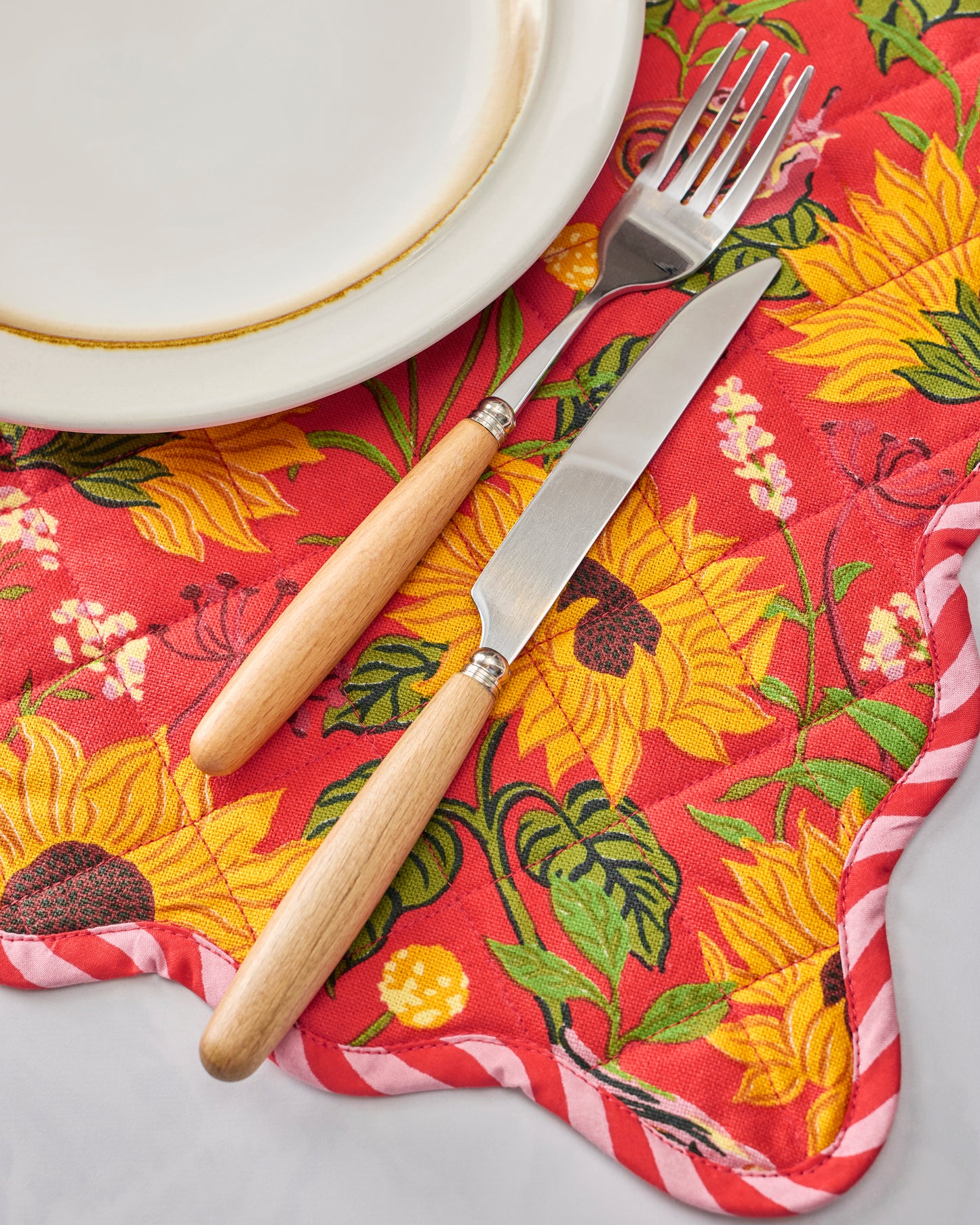 Close-up of orange quilted placemats with sunflower print, shown with a white plate, fork, and wooden-handled knife.