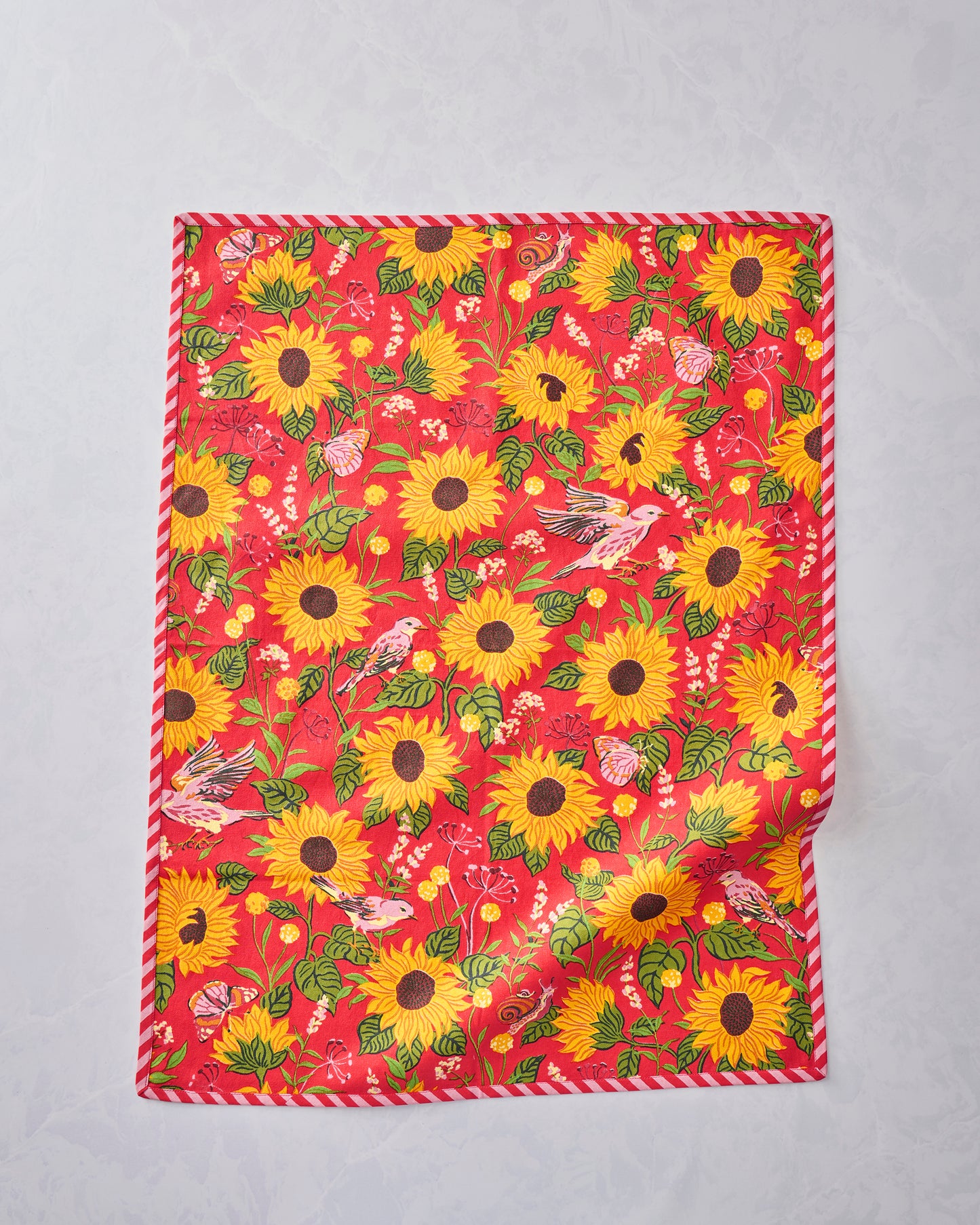 Tea towel displayed flat with an orange floral print featuring sunflowers, leaves, birds, butterflies, and a snail.