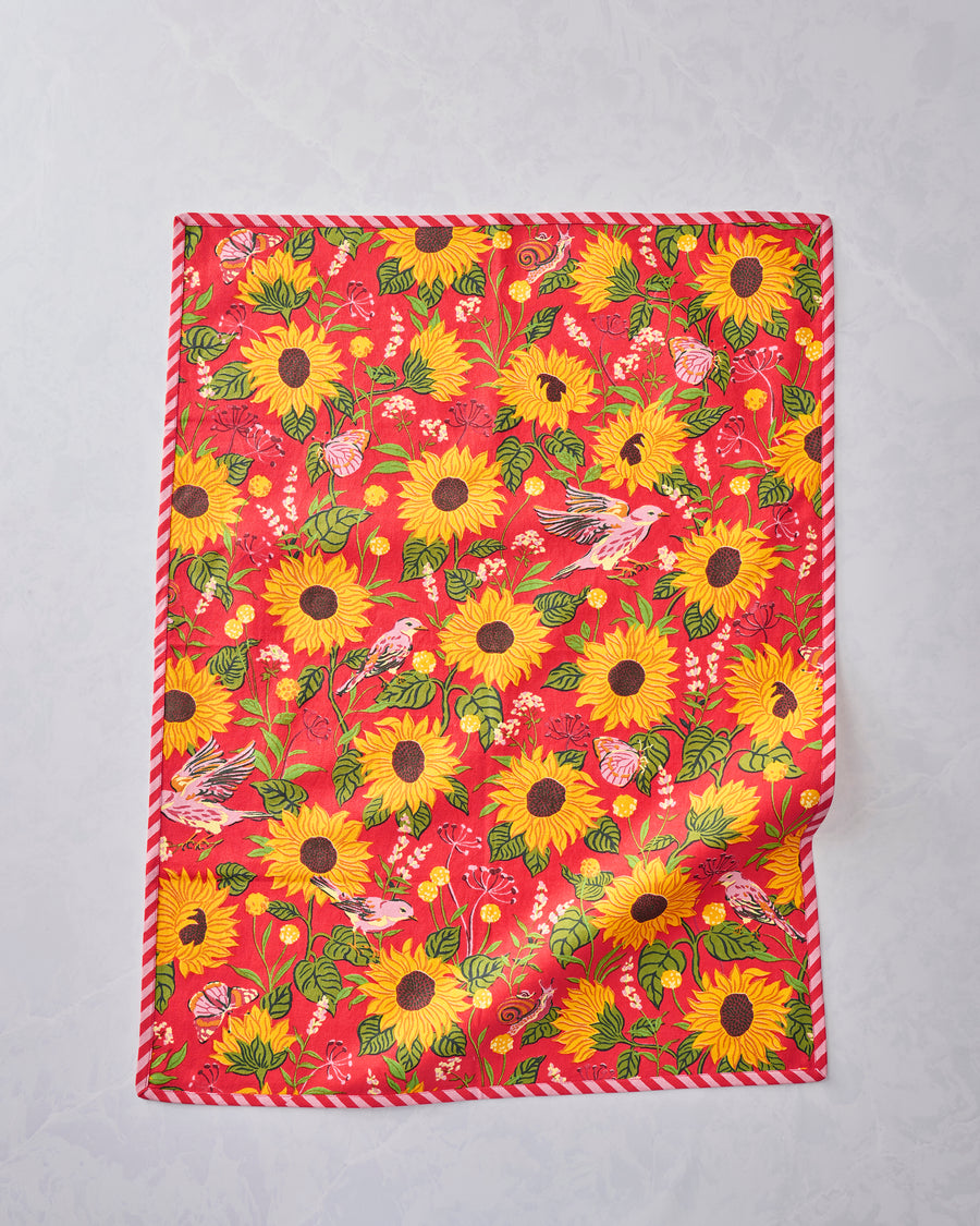 Tea towel displayed flat with an orange floral print featuring sunflowers, leaves, birds, butterflies, and a snail.
