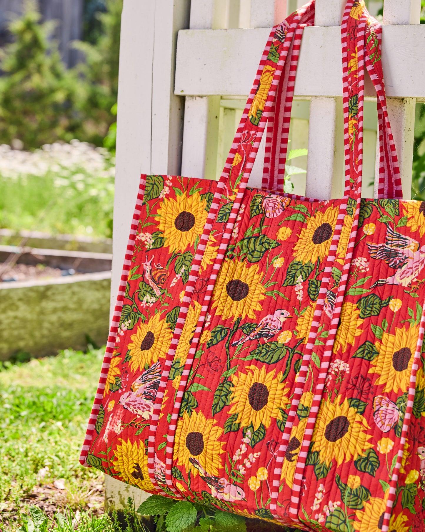 Quilted orange floral tote hanging on a white porch railing, with multiple pink-and-white striped handles.