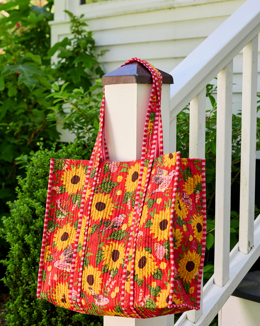 Quilted orange floral tote hanging from a porch post, viewed from the front and side to show its depth and striped handles.