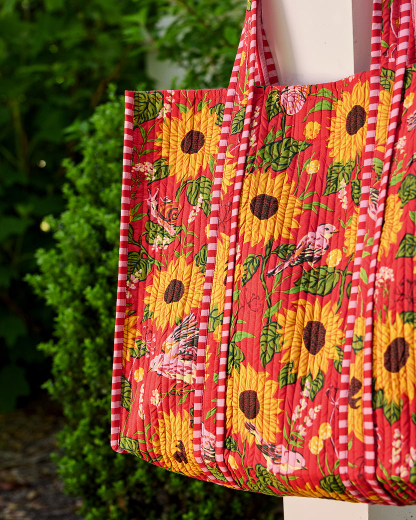 Close-up of the quilted orange floral tote showing sunflower, bird, and snail motifs with pink-and-white striped trim.