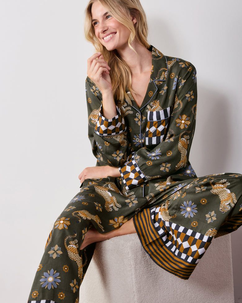 Seated front view of the olive tall Rittenhouse pajama set, showing the leopard and flower print, collared shirt, wide-leg pants, and checkerboard and striped trim.