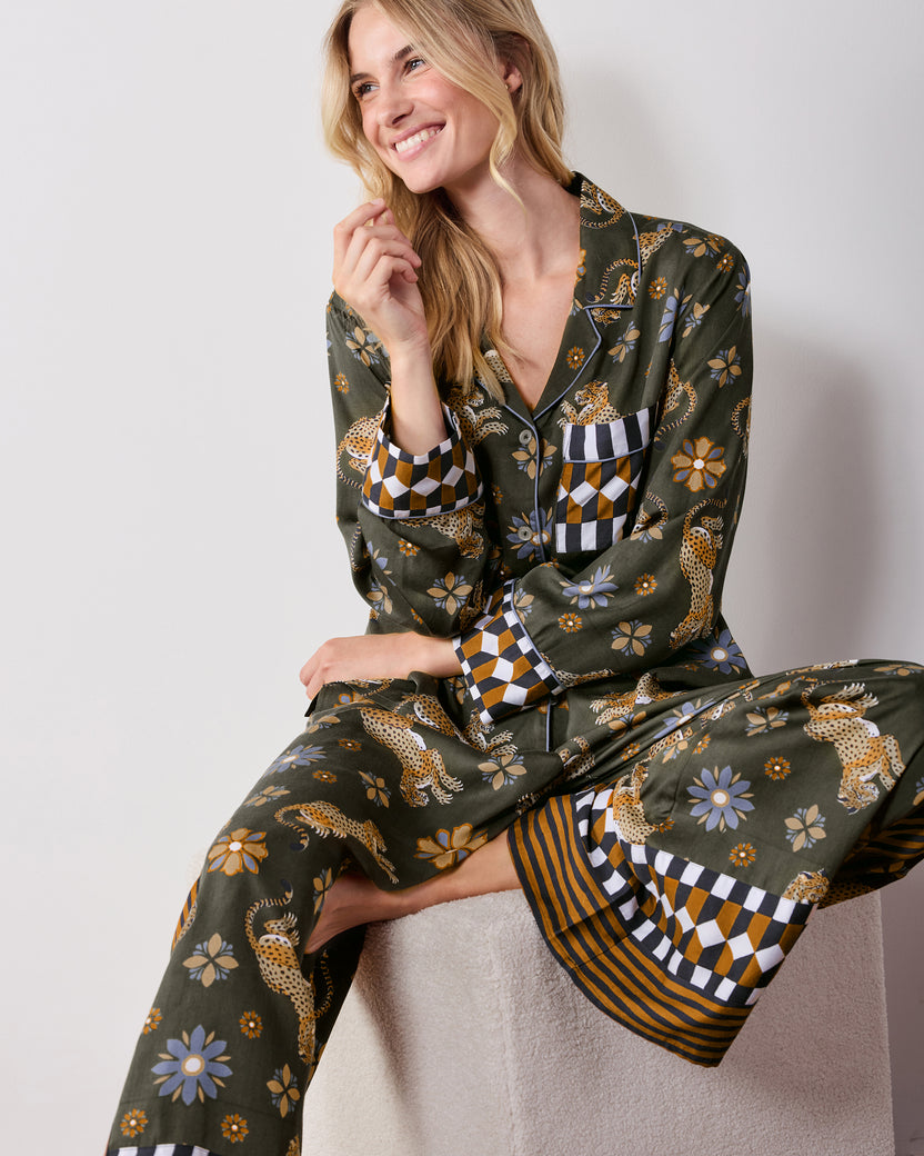 Seated front view of the olive tall Rittenhouse pajama set, showing the leopard and flower print, collared shirt, wide-leg pants, and checkerboard and striped trim.