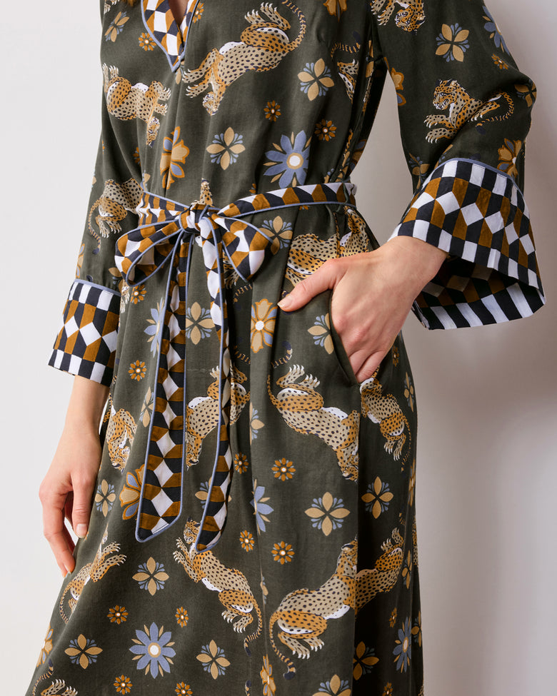 Close view of an olive caftan with spotted leopards, flowers, and geometric trim at the collar, cuffs, and belt.