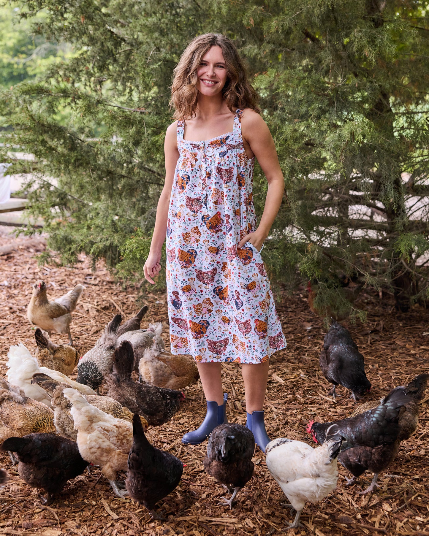 Person wearing a floral chicken-print sleeveless nightgown surrounded by chickens outdoors.