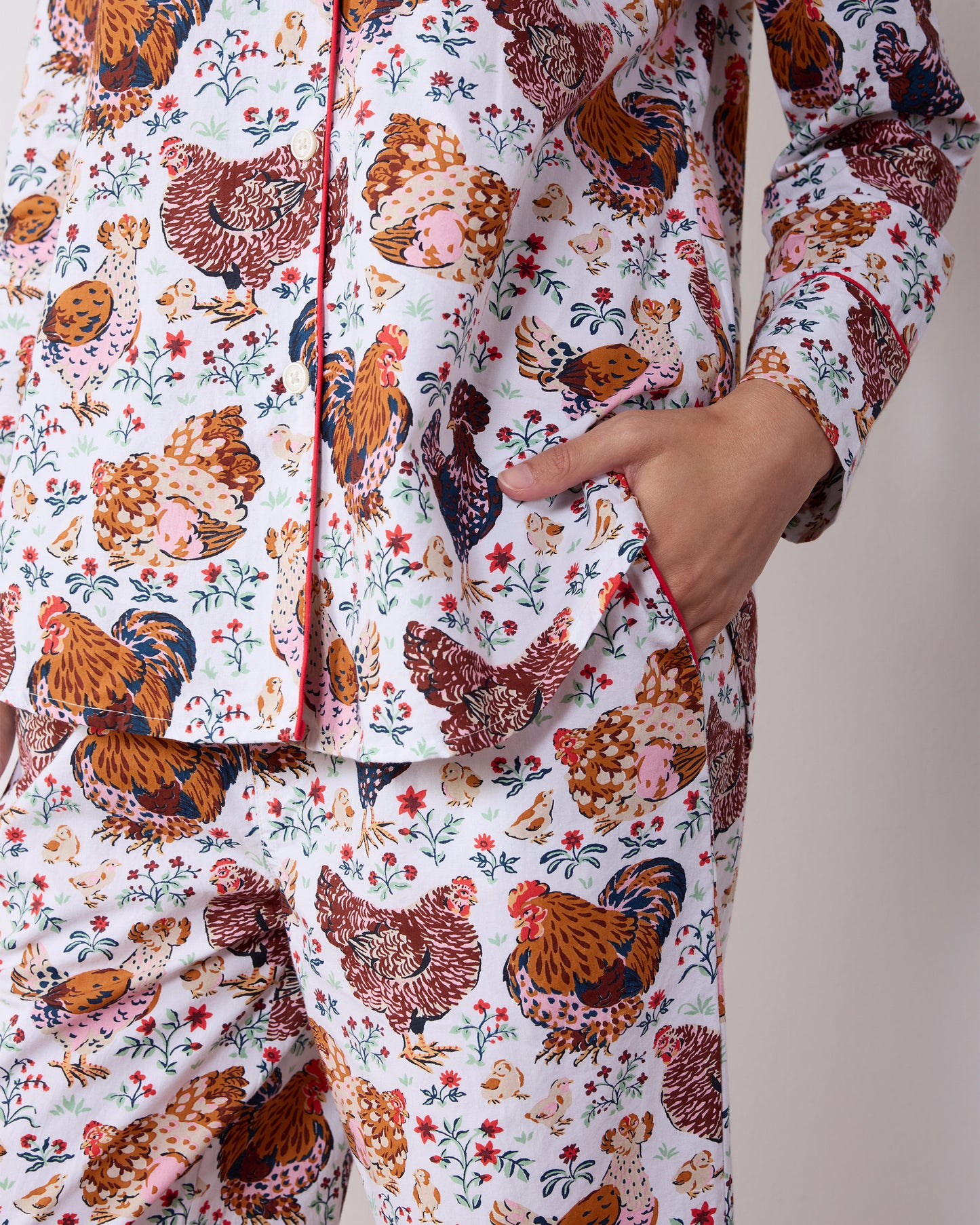 Close-up of a chicken-print long pajama set showing the button-front top, piping, and side pocket.