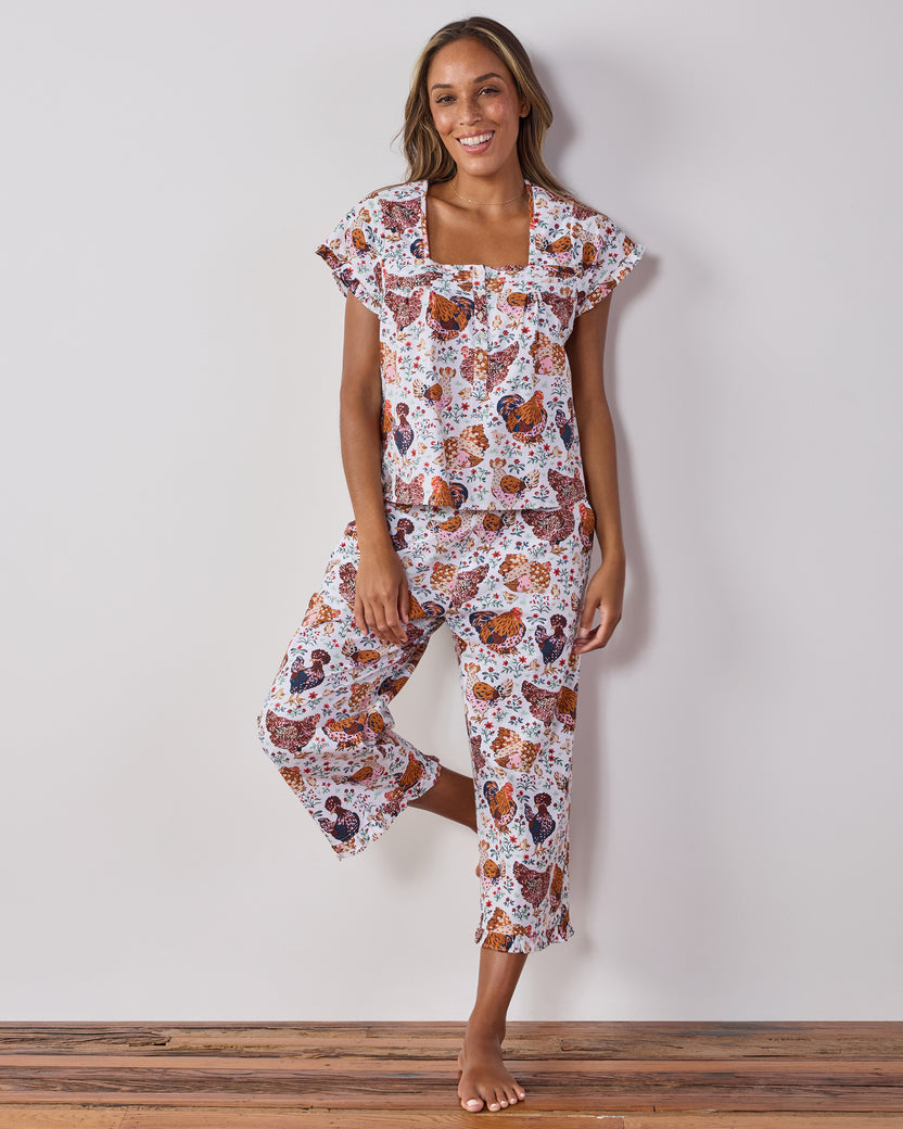 Front view of a person wearing a cropped short-sleeve top and cropped pants with a colorful chicken-and-floral print.