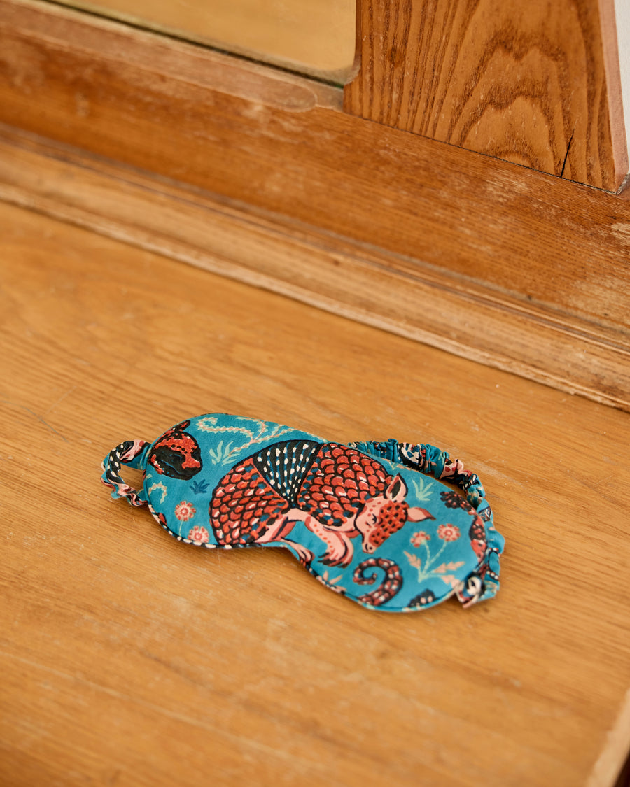 Teal Southwestern Critters eyemask displayed on a wooden floor, showing its printed front and elastic strap.