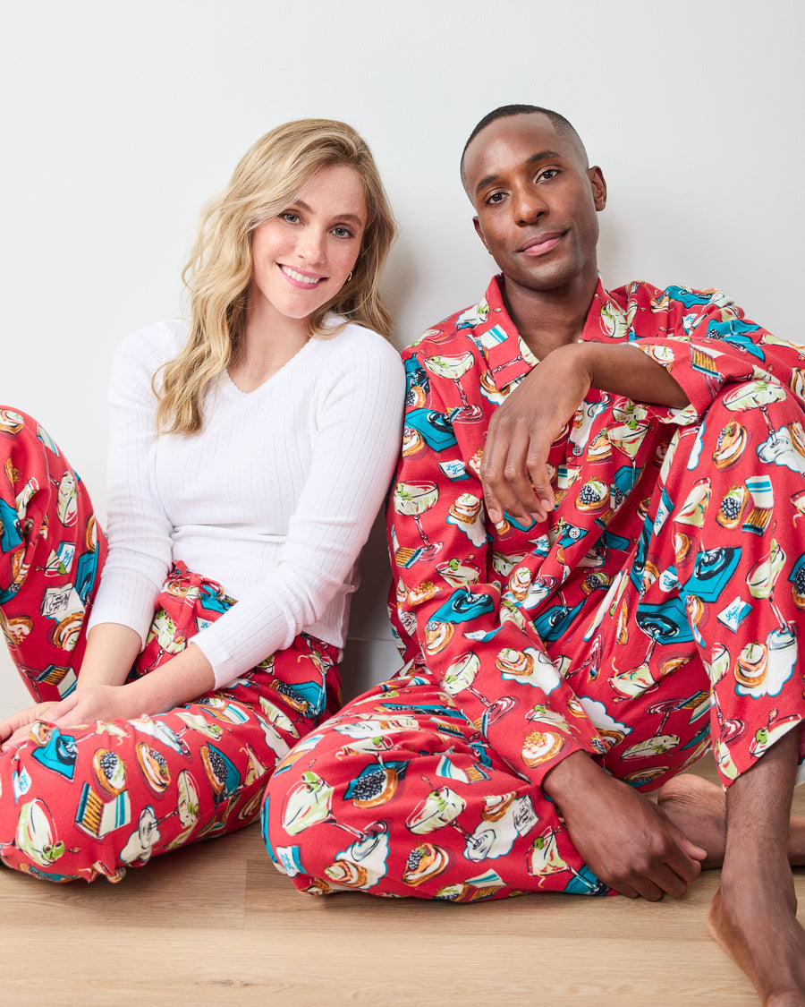 Two people seated in red printed pajama pants, with one wearing the matching button-down top