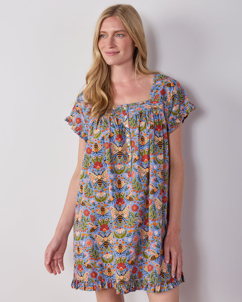 Person wearing the Delphinium Blue Bee Tapestry pintuck nightgown with short sleeves, a square neckline, and ruffled hem.