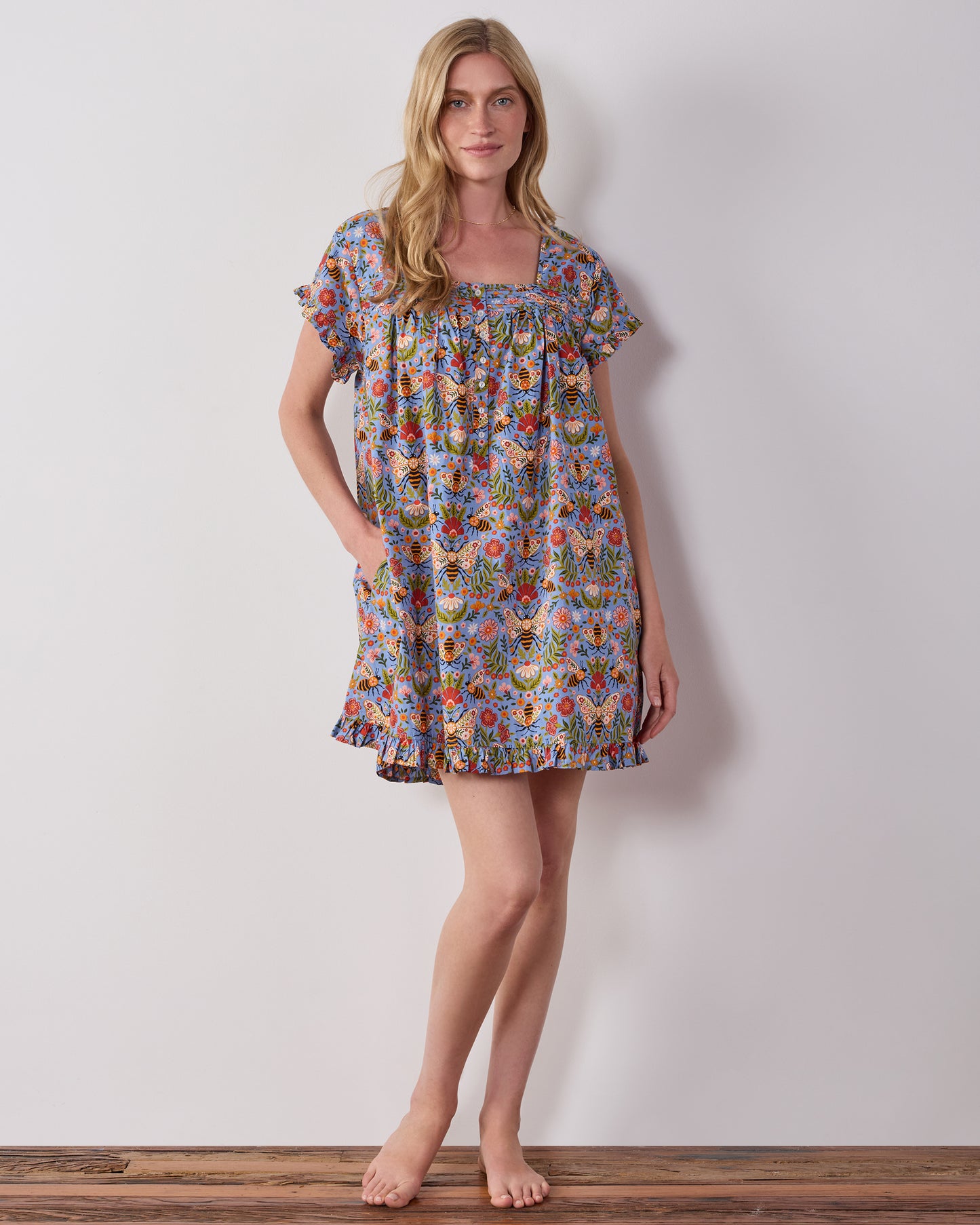 Model wearing the blue Bee Tapestry pintuck nightgown, shown from the front with short sleeves and a ruffled hem.