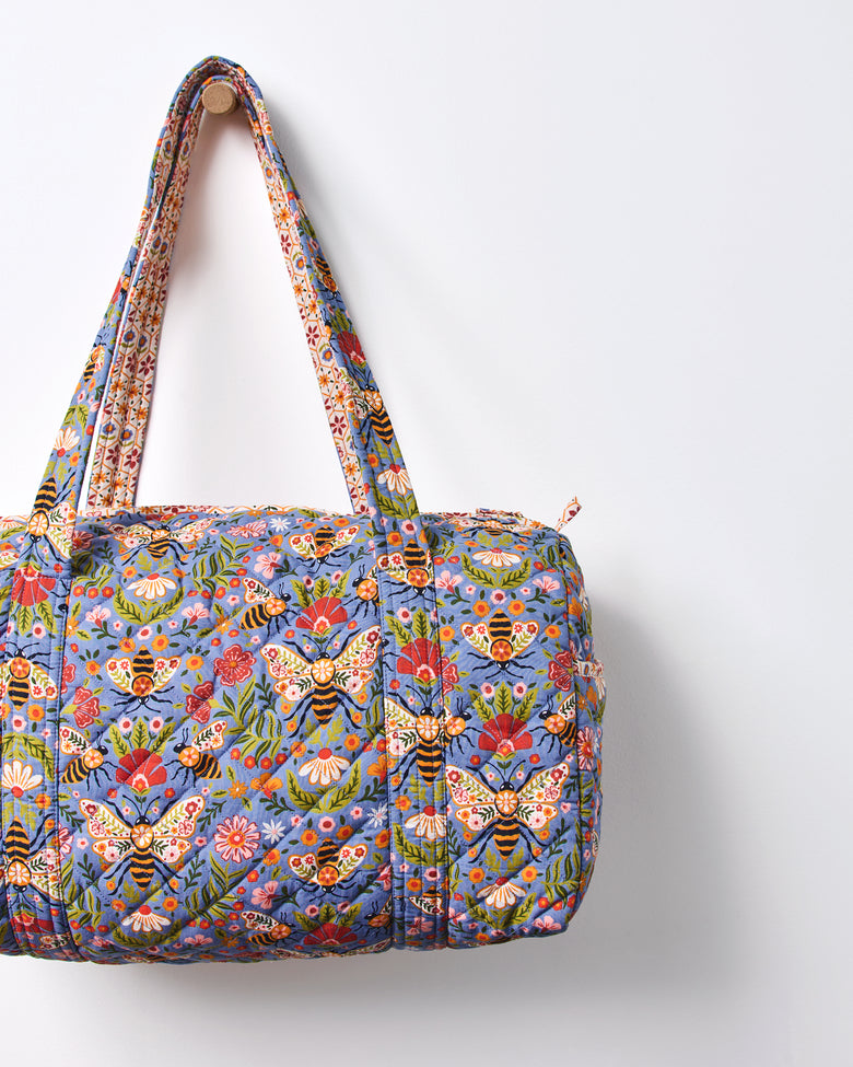 Close-up of the blue Bee Tapestry quilted duffle bag, showing its bee-and-floral print, handles, and top zipper.