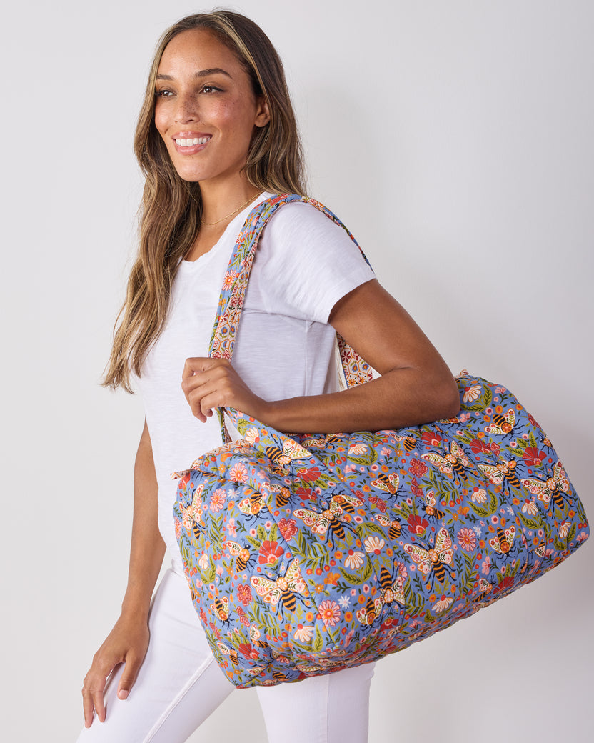 Person carrying the blue Bee Tapestry quilted duffle bag over one shoulder.