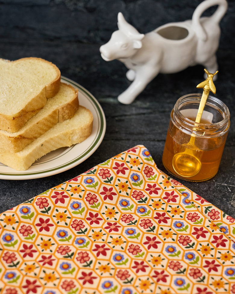 Bee Tapestry floral tea towel spread on a counter beside sliced bread and a jar of honey.