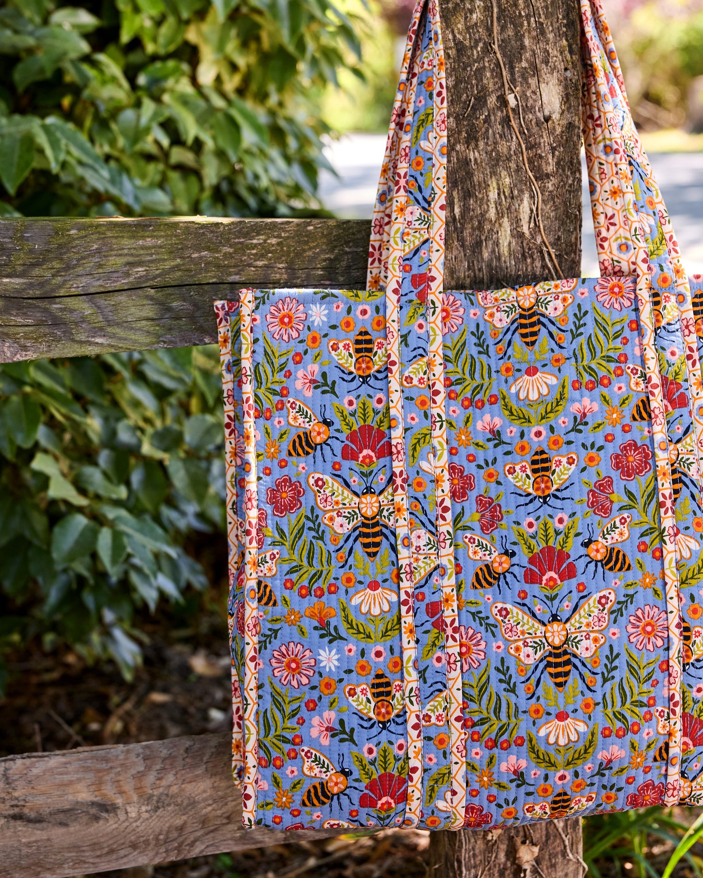 Close-up of the Bee Tapestry traveler tote showing its blue bee-and-floral print, handles, and side construction.