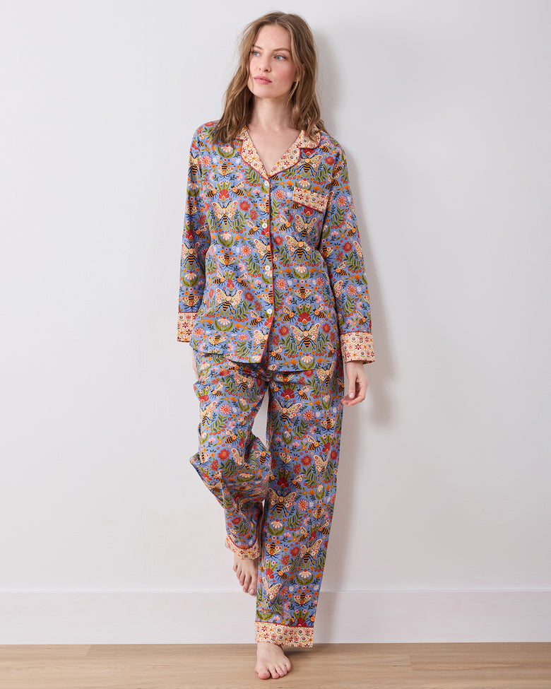 Full-length front view of a long-sleeve button-front pajama top and matching pants with a blue bee-and-floral print and contrasting collar, cuffs, and pant hems.