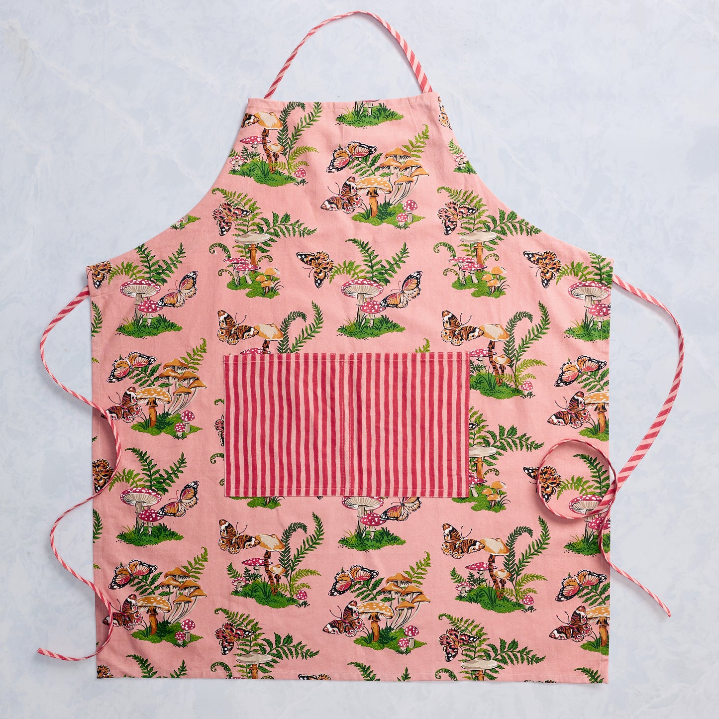Rosewood apron laid flat, with butterfly, mushroom, and fern print, adjustable neck strap, ties, and a striped front pocket.