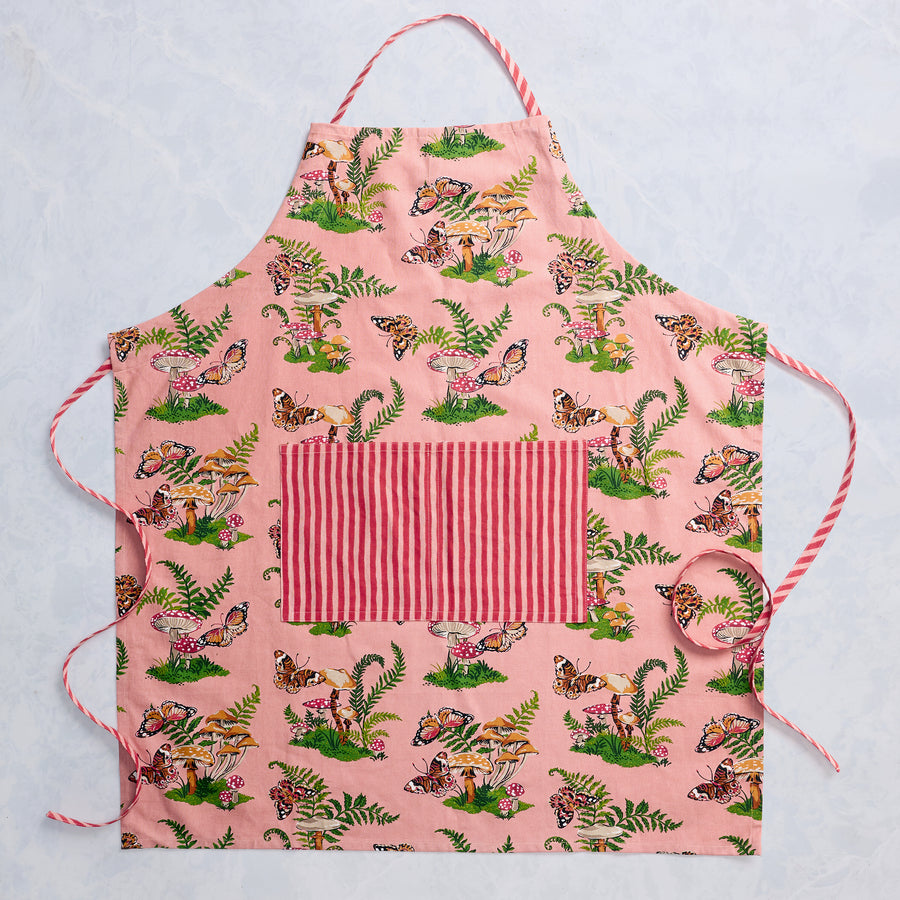 Rosewood apron laid flat, with butterfly, mushroom, and fern print, adjustable neck strap, ties, and a striped front pocket.
