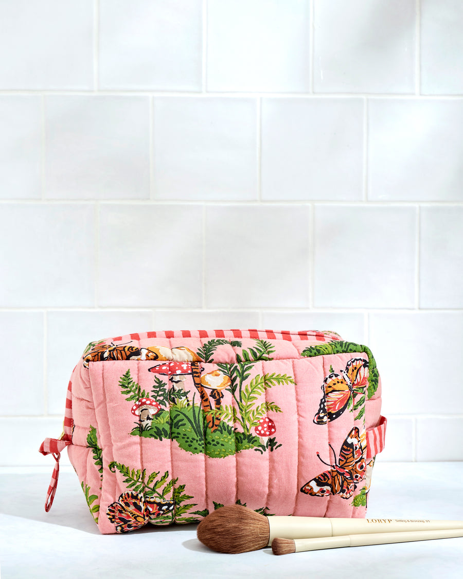Front view of a quilted butterfly-print pouch with mushrooms and ferns, shown beside makeup brushes.