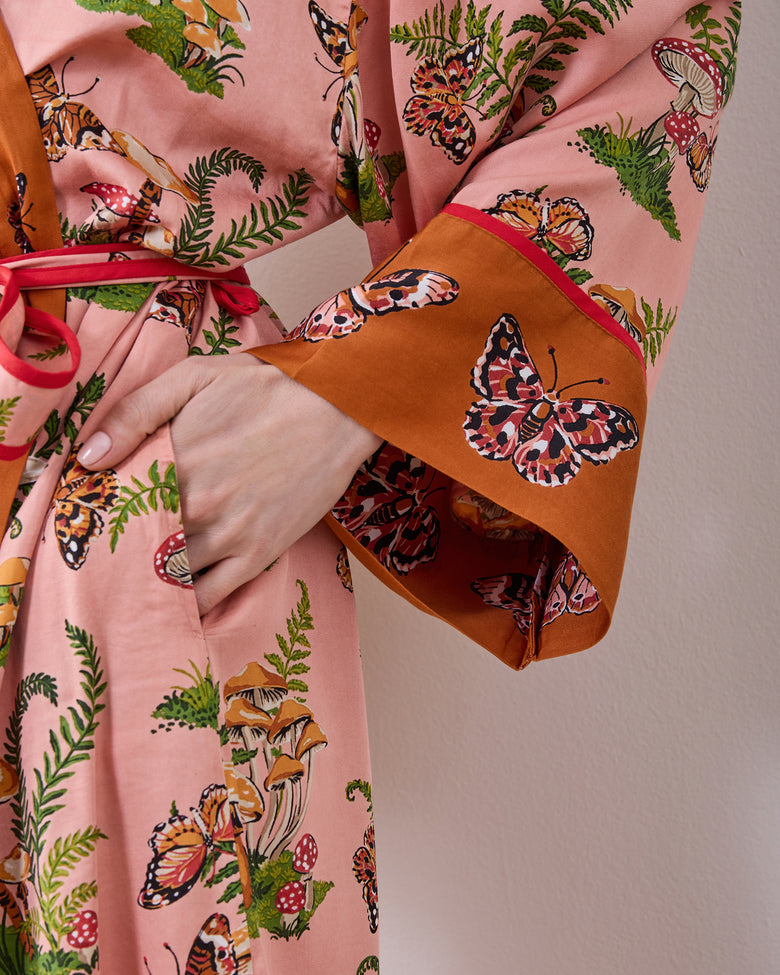 Close-up of the rosewood Butterfly Forager robe showing its printed sleeve cuff, pocket, matching tie, and butterfly, mushroom, and fern pattern.