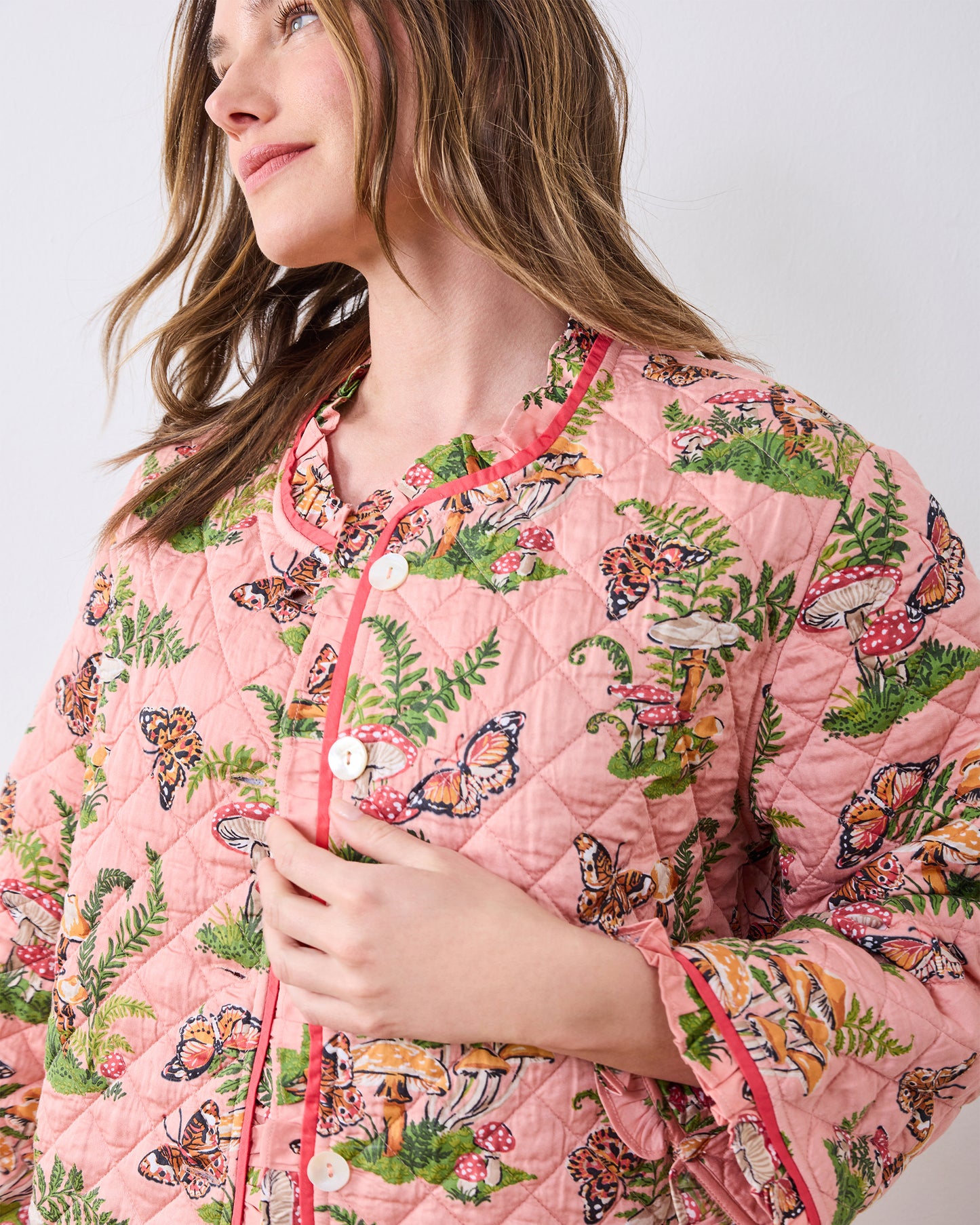 Close-up of the pink Butterfly Forager quilted slumber jacket showing its patterned fabric, ruffle-trimmed neckline, white buttons, and sleeve detail.