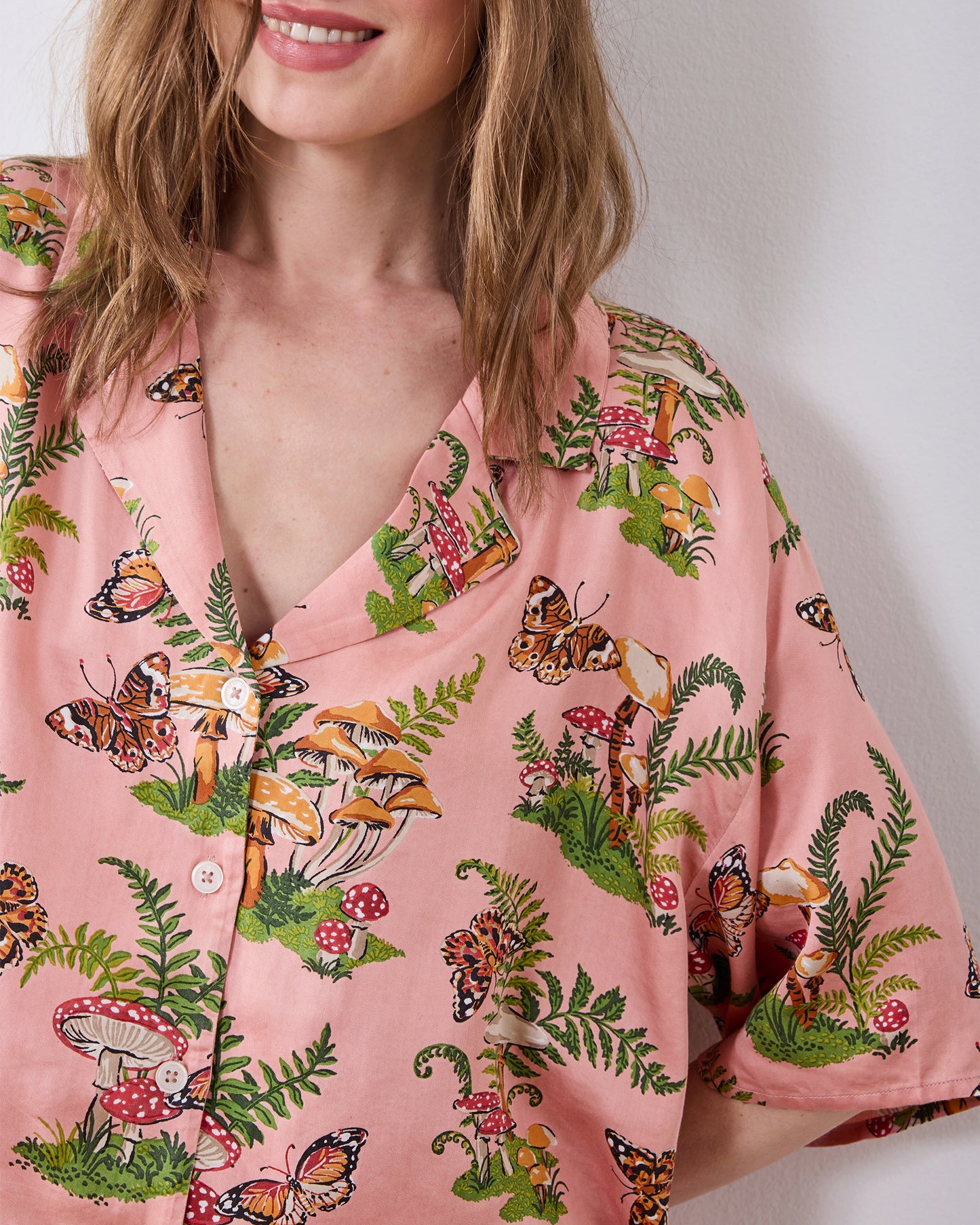 Close-up of the pink Butterfly Forager tall satin Wildest Dreams pajama top with a notched collar, buttons, and butterfly, mushroom, and fern print.