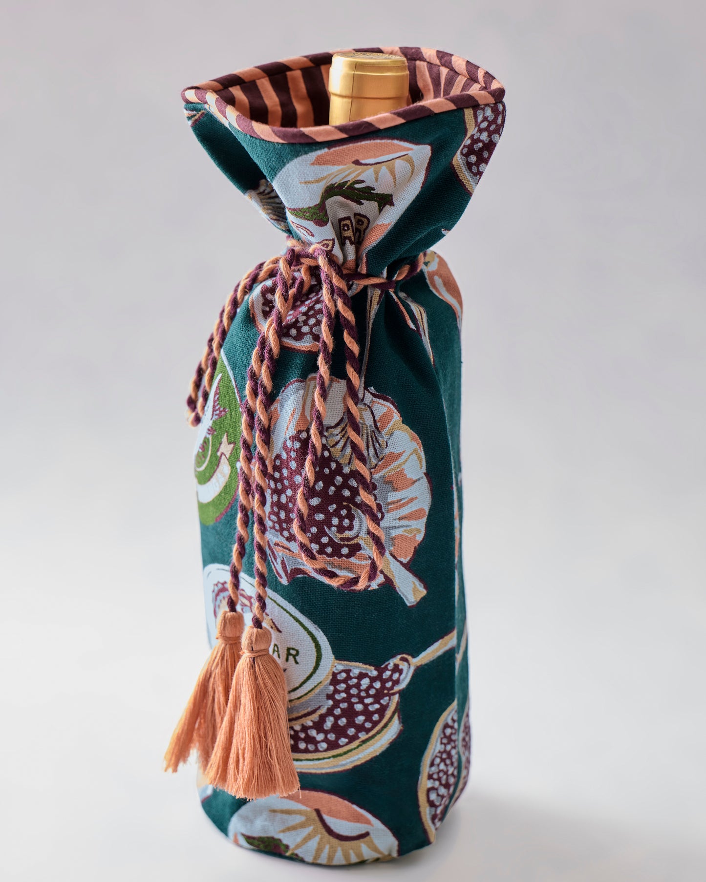Champagne & Caviar wine bag standing upright with a bottle inside, showing its patterned exterior, gathered top, braided tie, and peach tassels.
