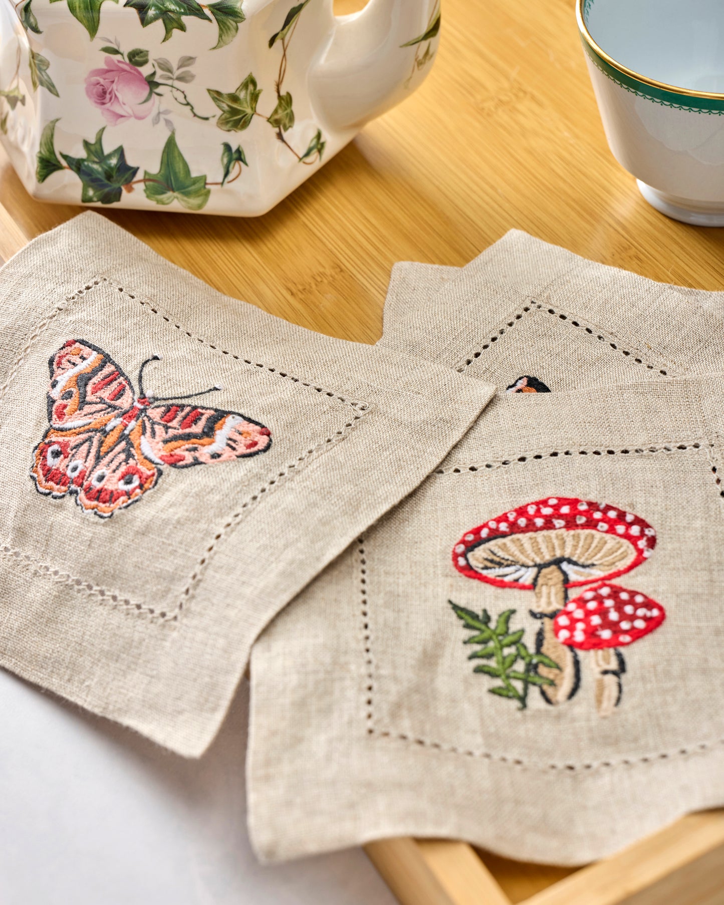 Close view of four embroidered cocktail napkins with butterfly and mushroom designs arranged on a table.