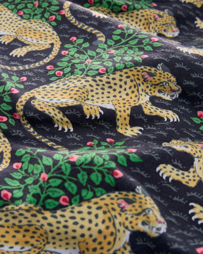 Close-up of black pajama fabric featuring repeated spotted leopard illustrations and green leafy branches with pink flowers.