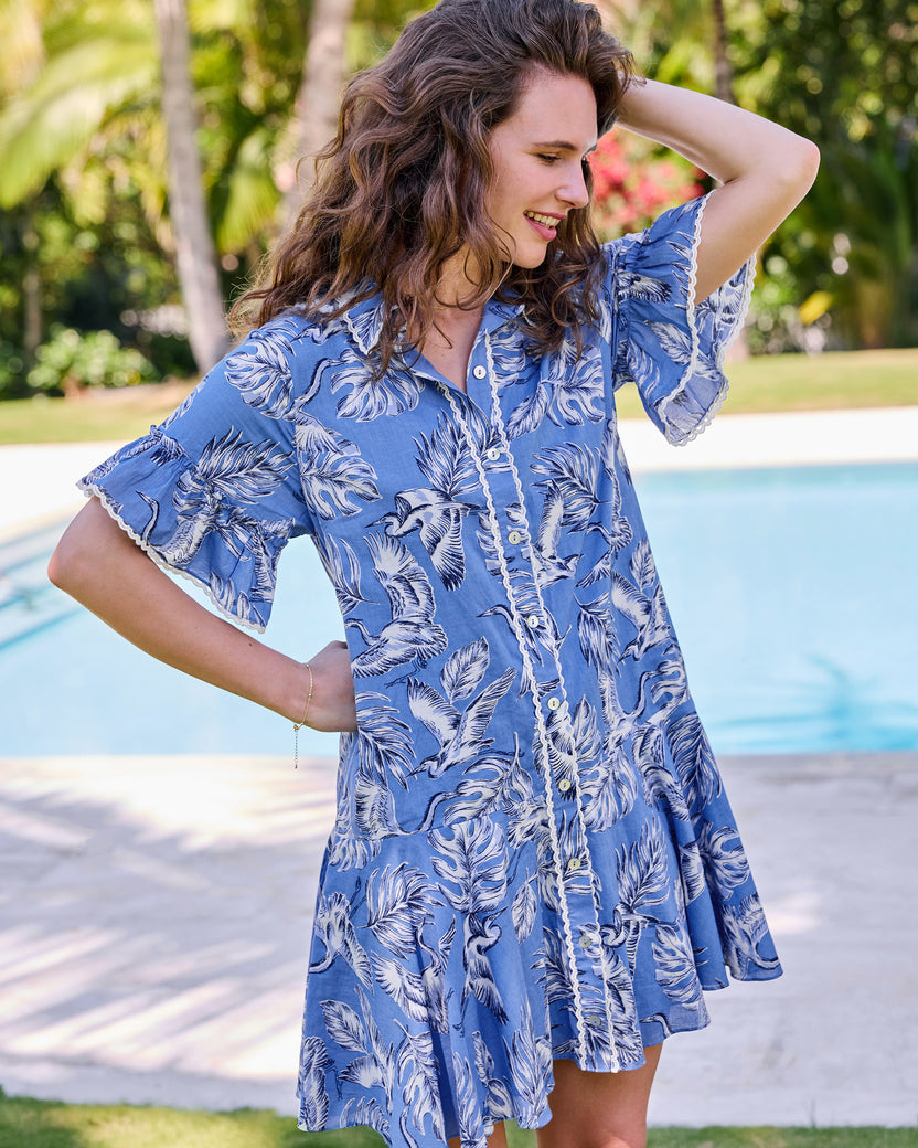 Angled view of the saltwater blue Estelle Dress showing the heron and palm print, button front, and ruffled sleeves
