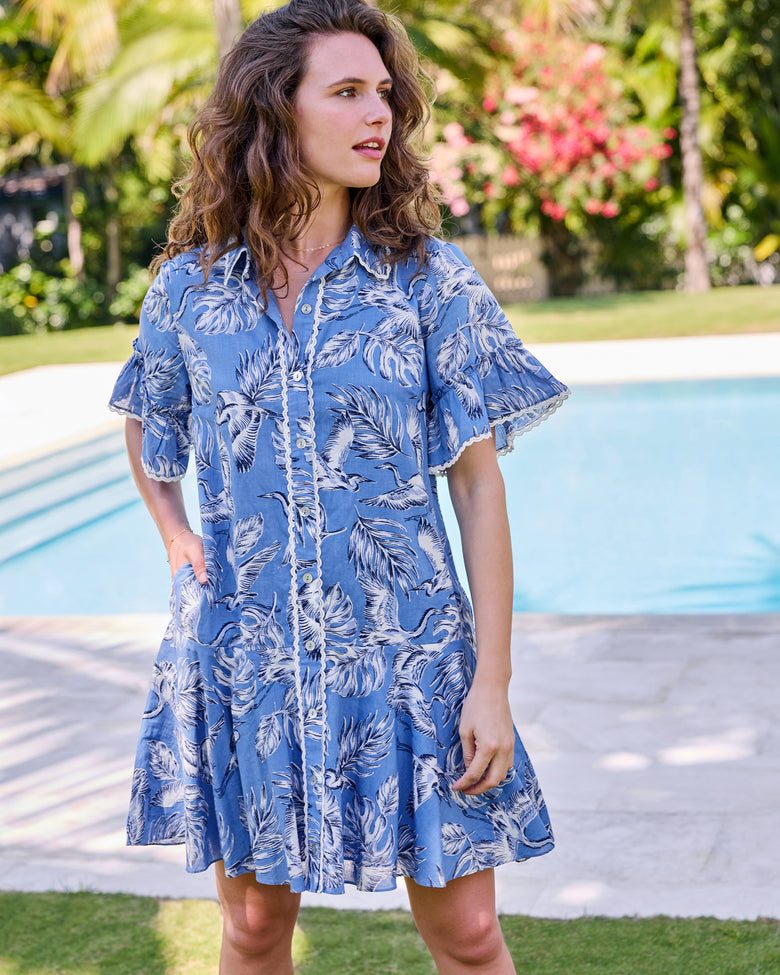Front view of the saltwater blue Estelle Dress with heron and palm print, button front, collar, and ruffled sleeves