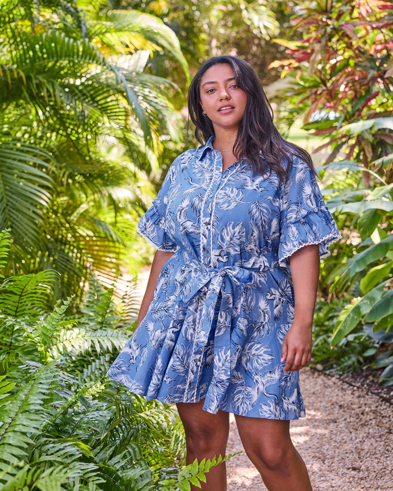 Full front view of the blue Estelle Dress with heron and leaf print, button front, ruffled sleeves, and tied belt