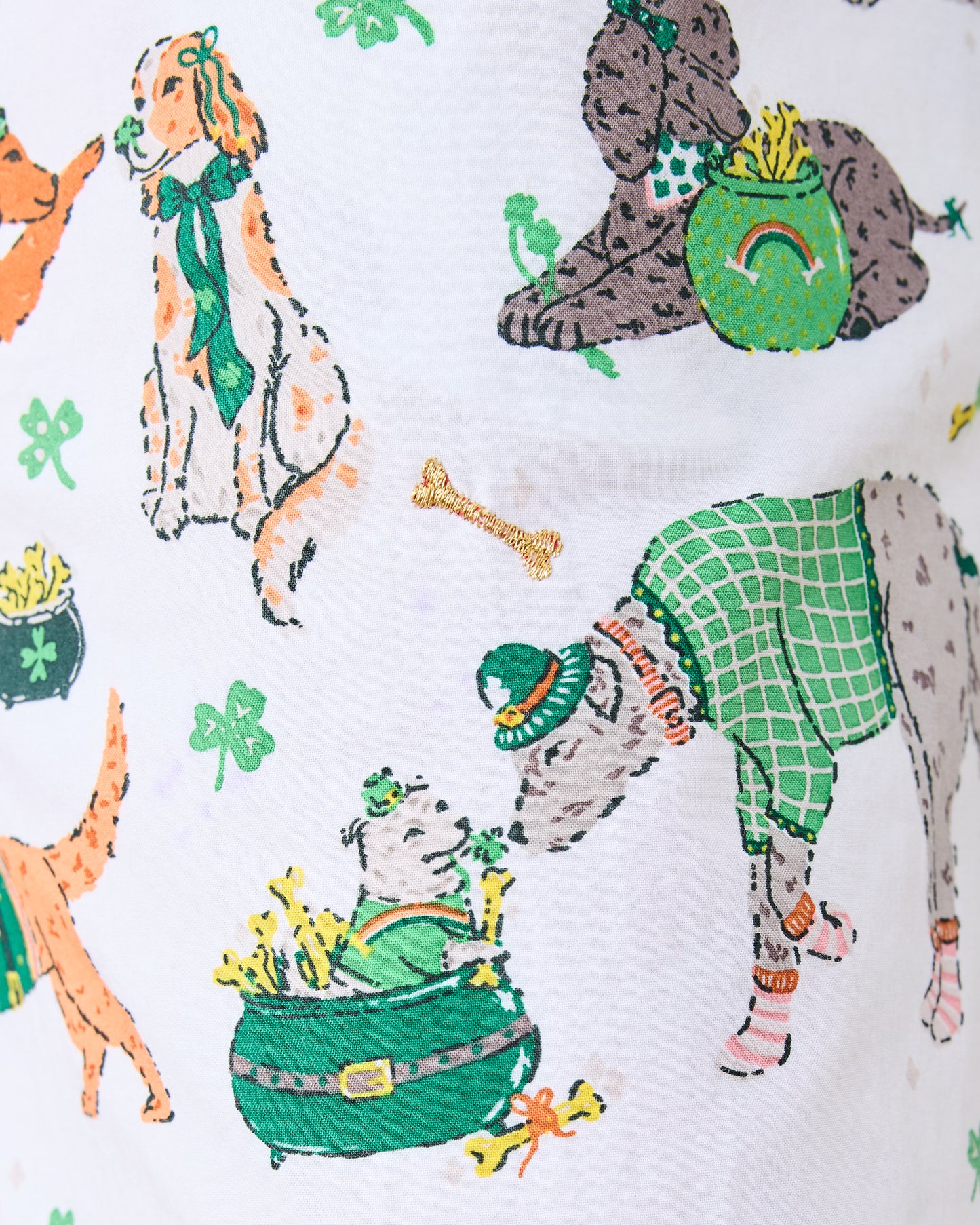 Close-up of the pajama print with dressed dogs, clovers, pots, rainbows, and an embroidered gold bone