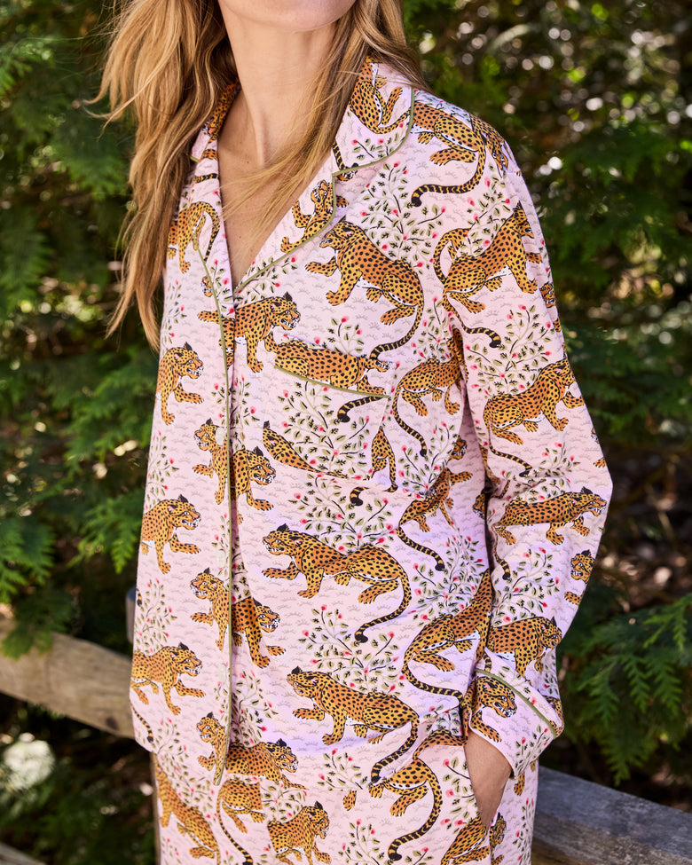 Close view of a person wearing a pink button-front long-sleeve pajama set with a leopard-and-floral print, standing outdoors.