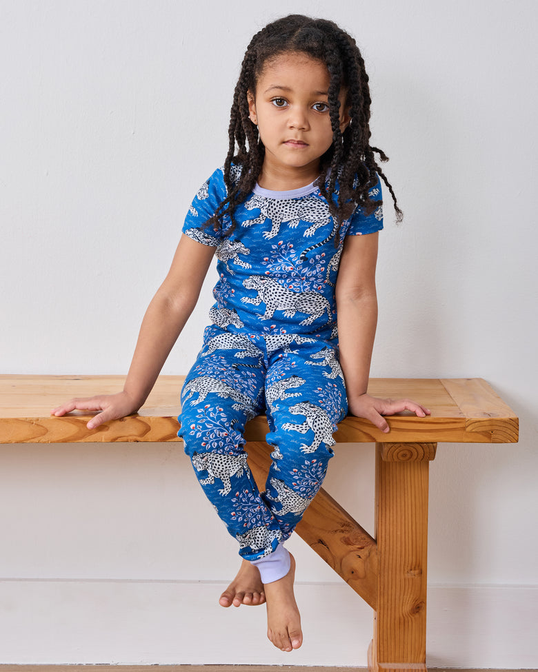 Model seated on a wooden bench wearing the indigo Bagheera short-sleeve pajama set