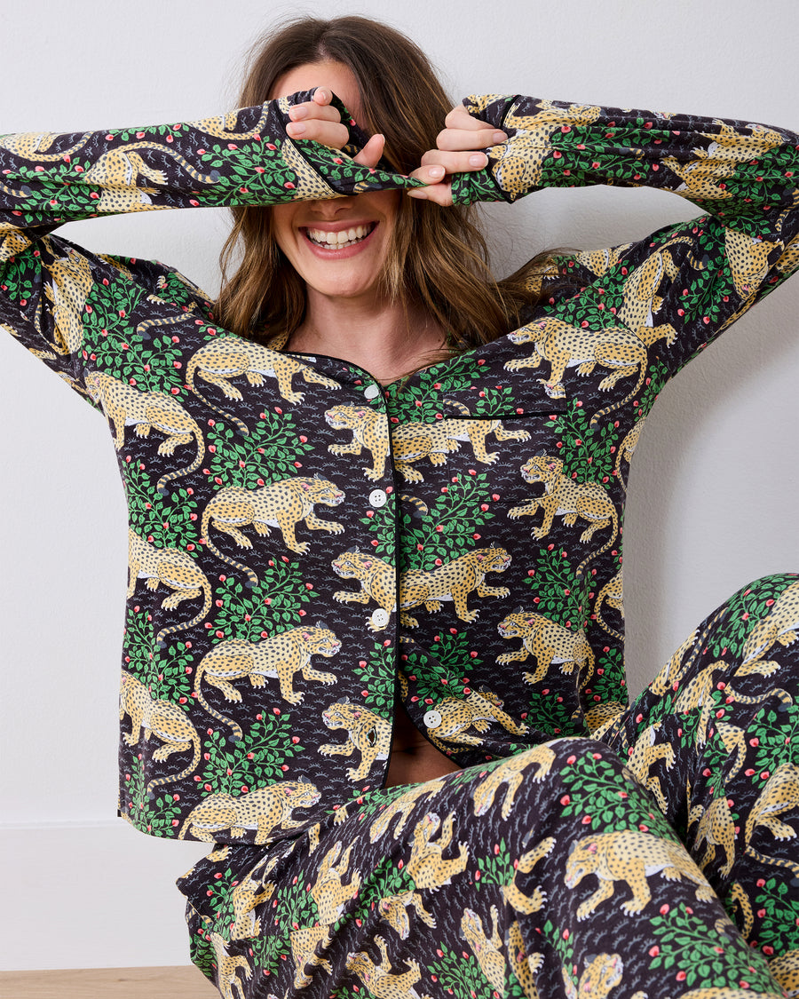 Person wearing a long-sleeve button-front pajama set with a leopard-and-leaf print, seated with hands covering the eyes.