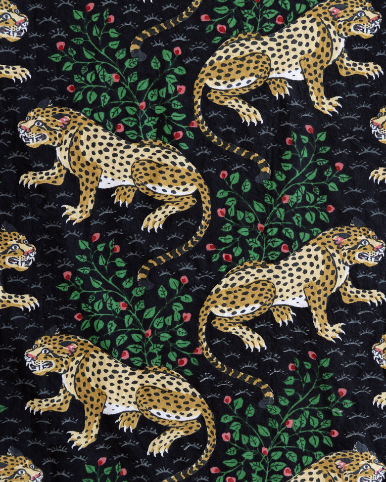 Close-up of the Bagheera print with spotted leopards, leafy branches, and red flowers on a black background